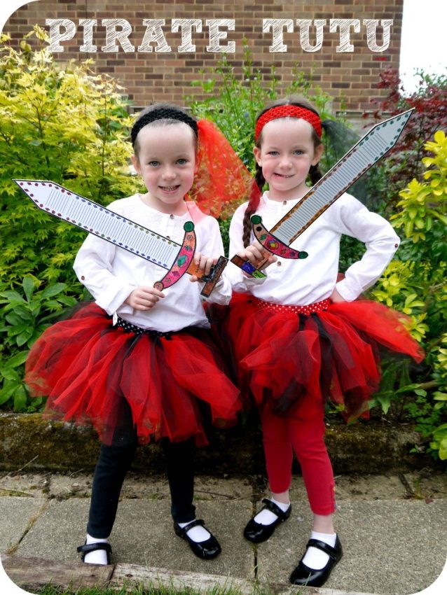 Two young children dressed in pirate costume and red kids’ tutus, holding toy swords and smiling at the camera. They wear white tops, black shoes, headbands, and stand outdoors beside green bushes. The text PIRATE TUTU is at the top.