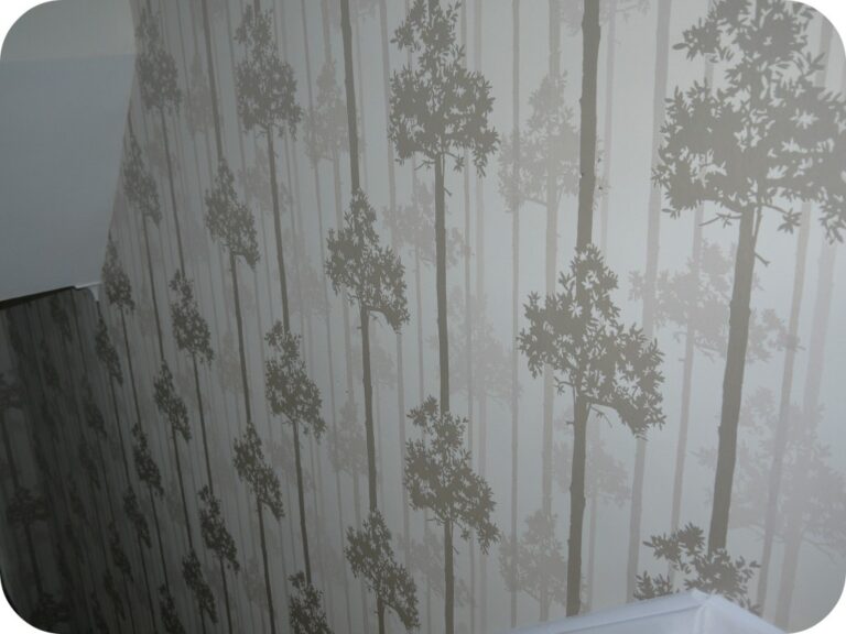 Superfresco Easy paste-the-wall wallpaper with a subtle forest pattern in shades of beige and grey, featuring tree silhouettes, covers the wall along a staircase with a white bannister.