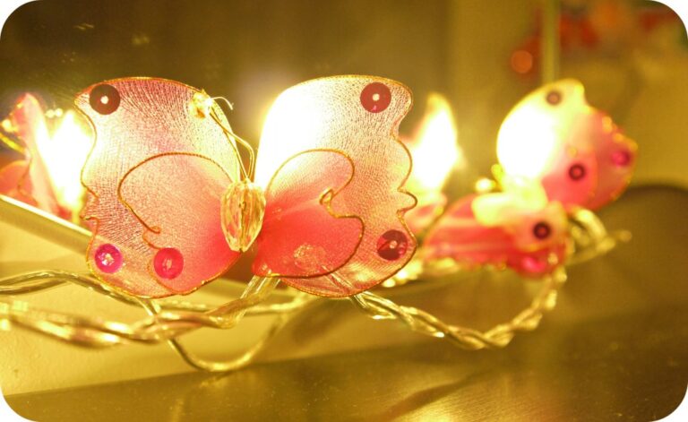 Close-up of Blaze On butterfly fairy lights glowing warmly on a twisted metallic wire. The cosy yellow light and sequin-detailed butterflies create a magical ambience—perfect for a twin girls' bedroom.