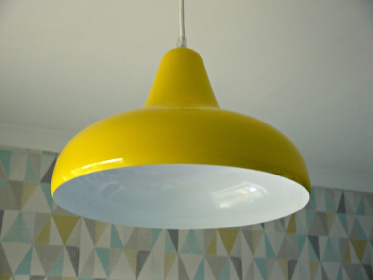 A yellow pendant light fitting with a white interior hangs from the ceiling, perfect as boys' bedroom lighting. The background features a wall with a geometric pattern of triangles in muted colours.