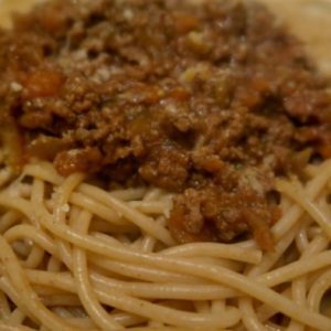 A close-up of cooked spaghetti topped with a chunky meat and tomato sauce, served on a white plate.