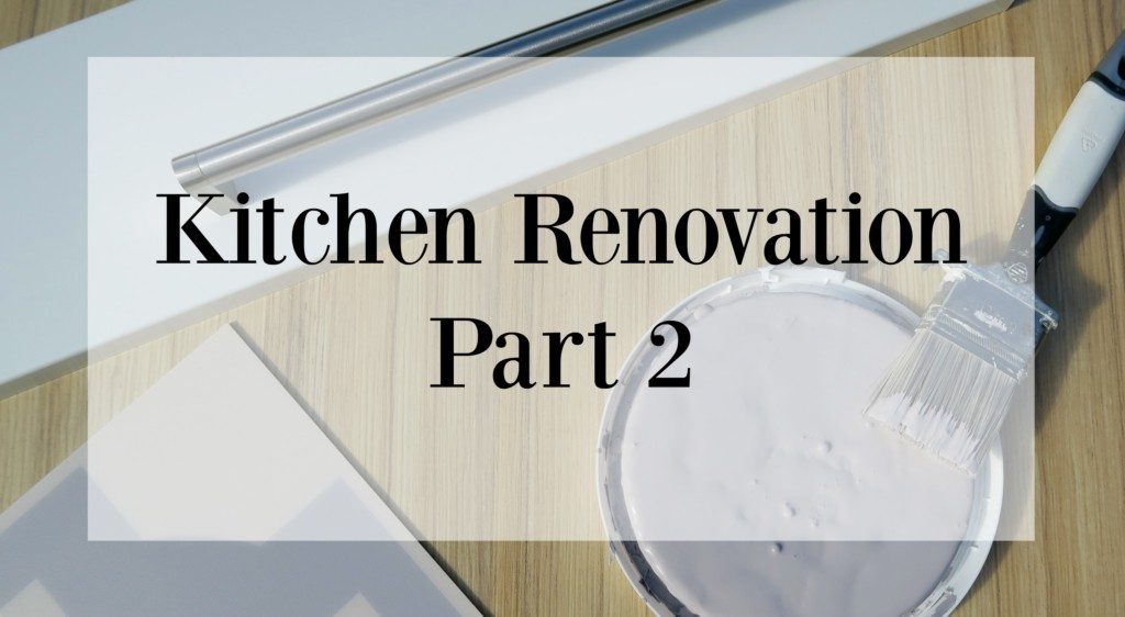 A paintbrush, a container of white paint, and renovation materials sit on a wooden table with the text Kitchen Renovation Part 2 boldly overlaid, highlighting the progress of your kitchen renovation journey.