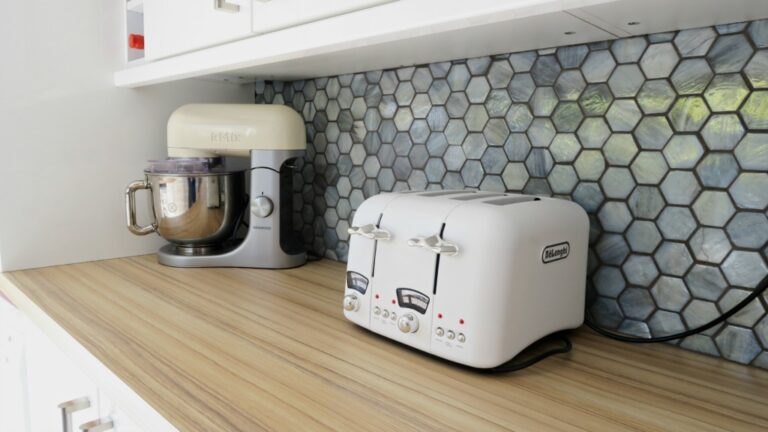 A white stand mixer and a white two-slot toaster sit on a light wood worktop in front of stunning blue glass mosaic tiles from Original Style, adding flair to this modern kitchen.