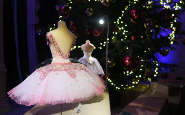 A pink and white beaded ballet costume is displayed on a mannequin at Mottisfont’s 12 Days of Christmas event, set before a festive tree with lights and baubles. Another tutu on a mannequin appears in the background.