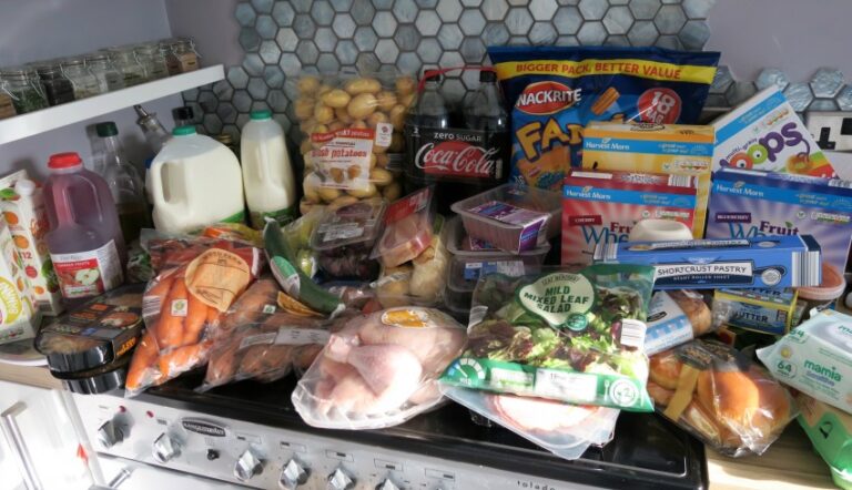 A grocery haul featuring fresh produce, milk, juice, snacks, bread, cereals, and packaged foods is spread out on the kitchen worktop and cooker—perfect for your weekly meal plan.
