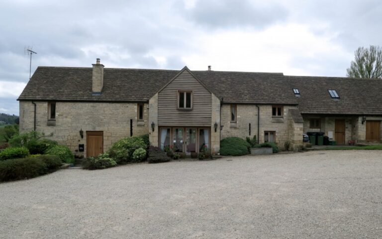 A large stone house with a gravel drive, gabled roof, and wooden central section sits among shrubs and greenery under a cloudy sky—captured during week 19 for our weekend in pictures series.