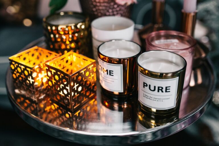 A round metal tray holds lit decorative lanterns, glass candles labelled TIME and PURE, and other small candles in glass holders, creating a warm, cosy ambience—perfect for stylish bedroom decor and fashionable motifs.