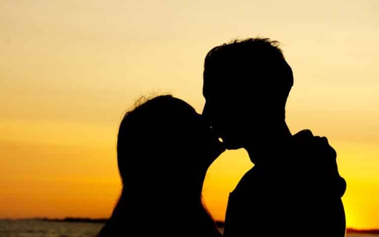 Silhouette of a couple kissing at sunset on West Witterings Beach, with an orange and yellow sky in the background, capturing a moment of pure fun and romance.