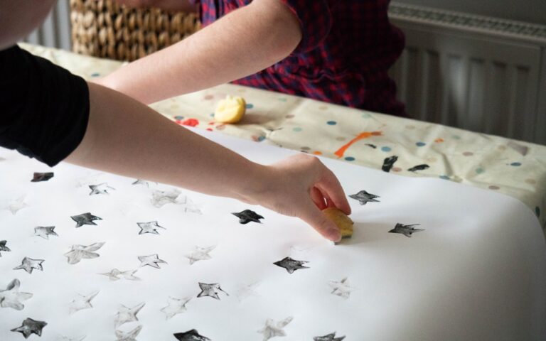 Two people use small objects to stamp black and grey stars on a large sheet of white paper, creating a star pattern—capturing a creative Weekend In Pictures moment at the crafting table.
