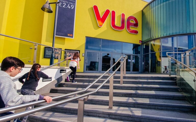 Three children are walking up steps towards the entrance of Vue Eastleigh cinema, with a bright yellow exterior and large red Vue sign above the doors—perhaps heading to see Dumbo for Mother’s Day.