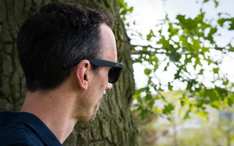 A man wearing black sunglasses stands outdoors, facing away from the camera—a perfect moment for a 2019 Father’s Day Gift Guide set among tree trunks, green leaves, and a softly blurred sky.