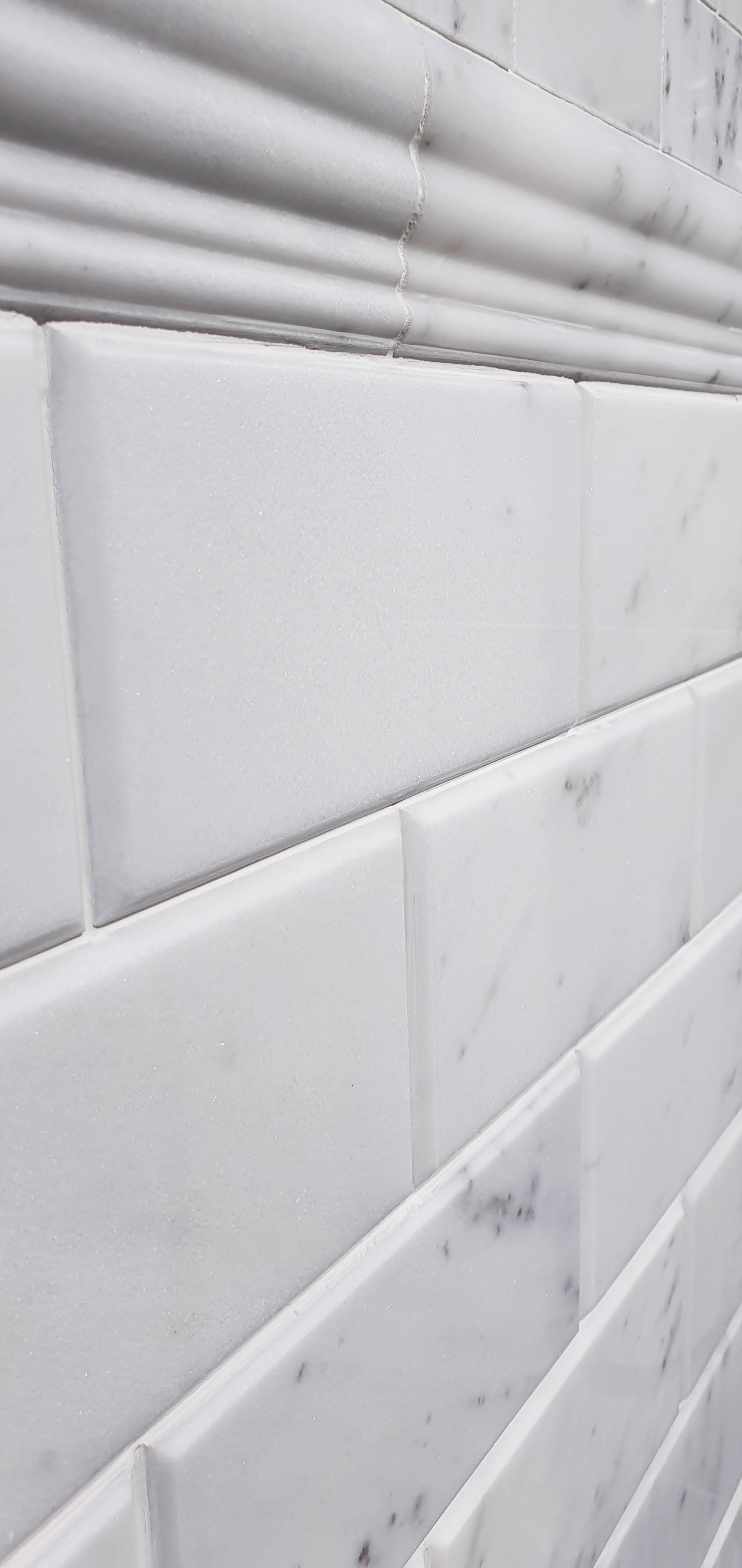 Close-up view of a white marble tiled wall with rectangular tiles and subtle grey veining, topped by a decorative moulding strip—perfect for inspiring shower or utility room ideas.