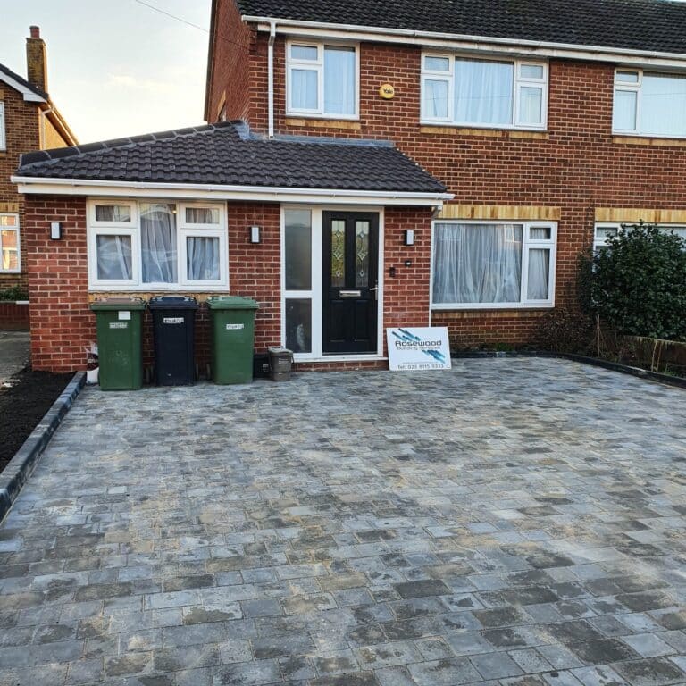 Big Update: A brick house with a newly laid drive, three green bins near the front door, and a sign for Norfolk Paving & Driveways—plus room for a future house extension—all visible from the window.
