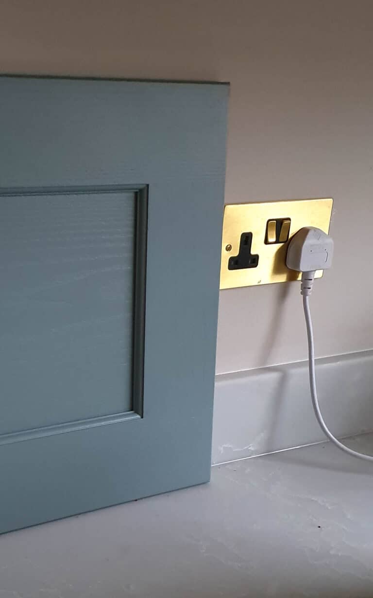 A blue cupboard door, part of a recent house extension, partially blocks a wall socket, with a white plug awkwardly inserted into the socket behind the door.