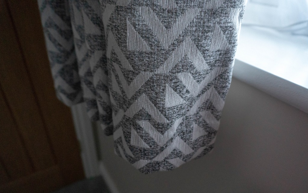 A close-up of a grey and white fabric with a geometric zigzag and chevron pattern, perfect for a navy bedroom or teenage boys’ space, hanging near a white windowsill in a softly lit room.
