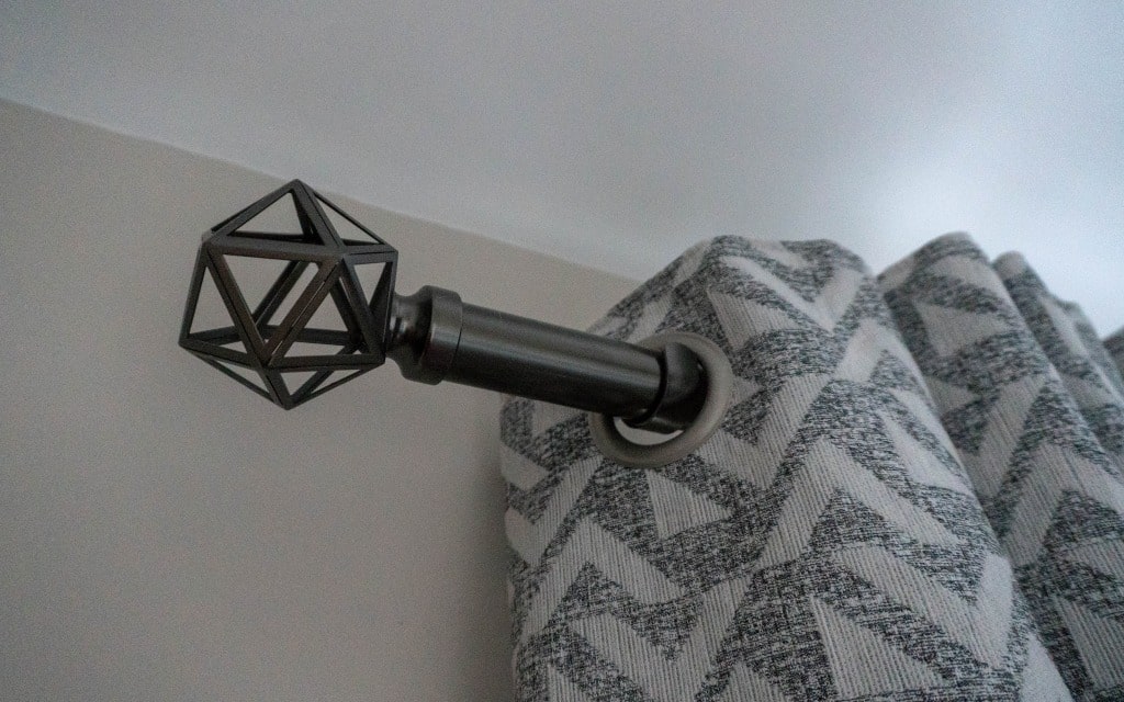 A geometric metal curtain rail with a black, polygon-shaped finial holds up grey and white patterned curtains, adding a bold accent to a teenage boys' bedroom or navy bedroom with light-coloured walls and ceiling.