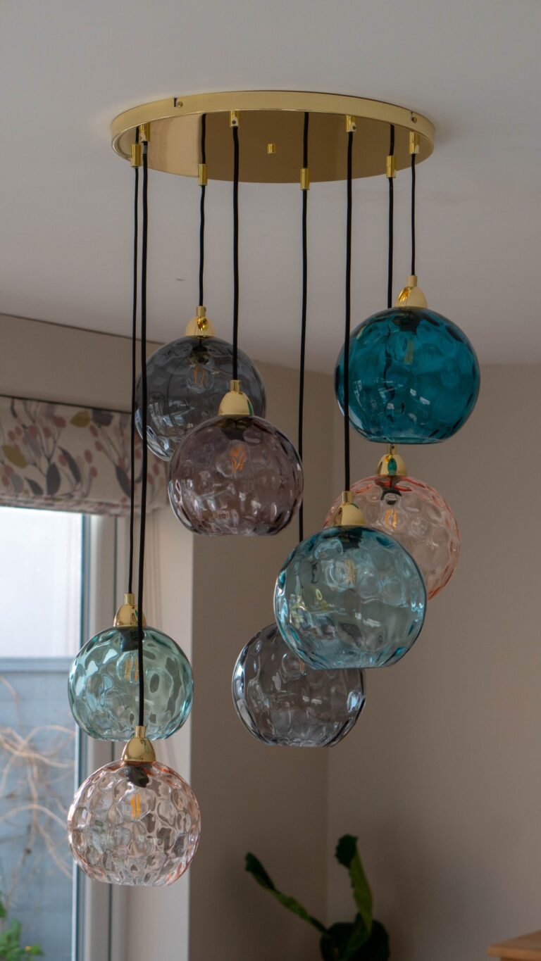 A modern chandelier with eight textured glass globes in blue, grey, and pink hues hangs from a gold ceiling plate on black cords, perfect for your Blue and Gold Kitchen or as a statement piece in your Dining Room Reveal.