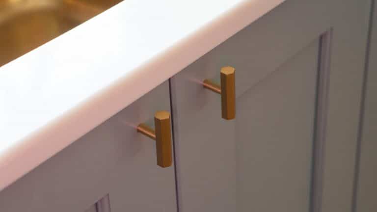 Close-up of two light grey cupboard doors with gold hexagonal knobs beneath a white worktop in a stunning Blue and Gold Kitchen.