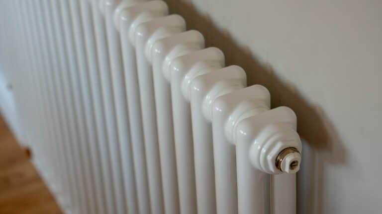 A close-up view of a white, metal radiator attached to a beige wall in the dining room, with horizontal sections and a valve visible at the top right.