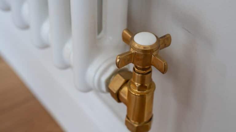 Close-up of a brass radiator valve attached to a white radiator against a light-coloured wall, with a wooden floor partially visible—perfect for your Dining Room Reveal.