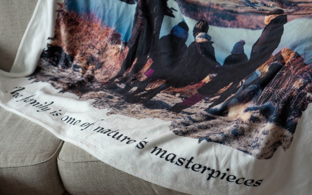 A blanket featuring a group of people outdoors and the text "The family is one of nature’s masterpieces," draped over a light-coloured sofa—a perfect Mother’s Day gift inspired by timeless moments and featured in our 2020 Gift Guide.