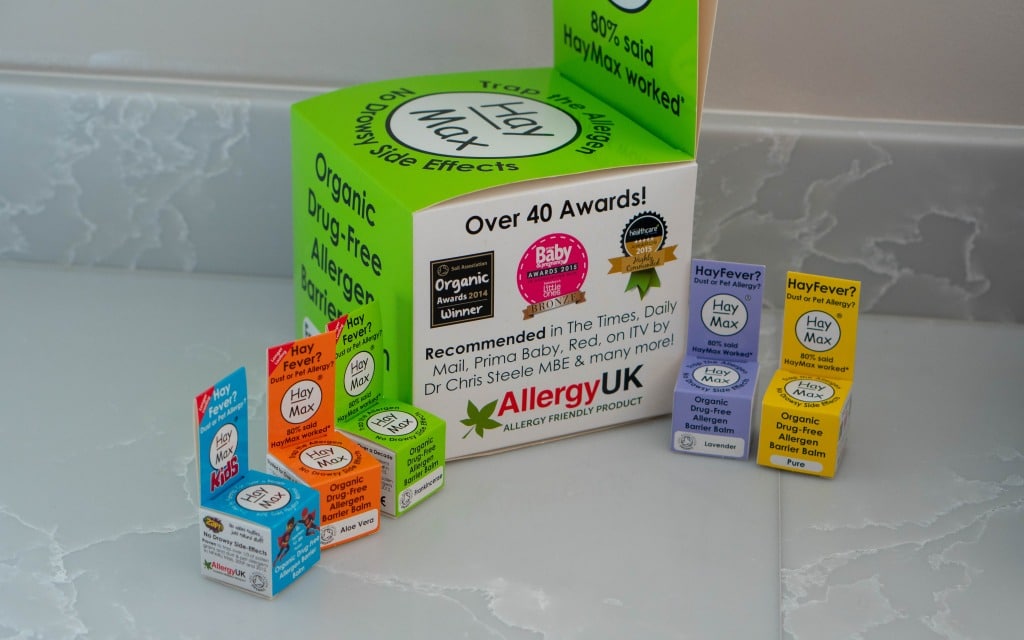 Display of HayMax organic allergen barrier balm boxes in various colours arranged on a counter, with a larger green promotional box in the background highlighting awards and Allergy UK endorsement—a helpful choice for home education and children’s education.