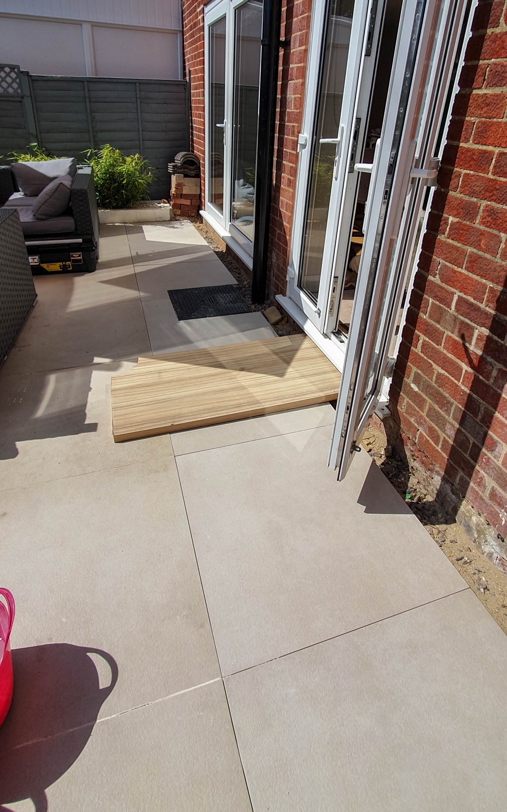 A temporary wooden ramp leads from a tiled patio into a house with open glass doors, providing accessible entry. Outdoor seating offers a relaxing spot to enjoy the garden views and monthly gardening activities in May’s fresh air.