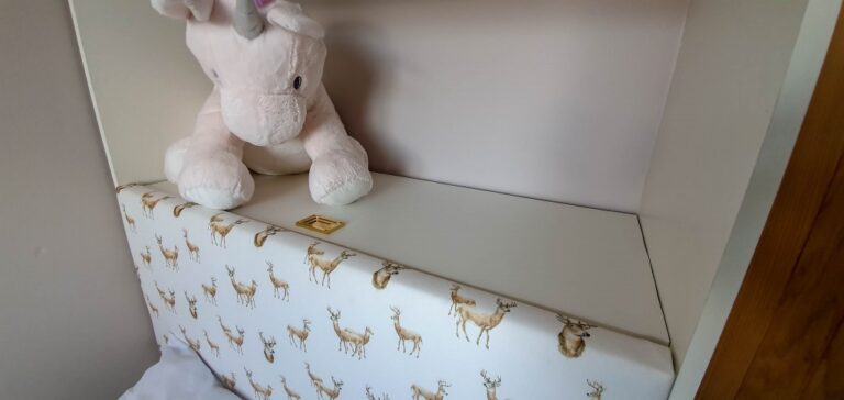 A stuffed pink unicorn toy sits on a white shelf above a rectangular cushion decorated with a deer pattern, adding charm to this Small Bedroom. A small gold object rests on the flat surface next to the toy.