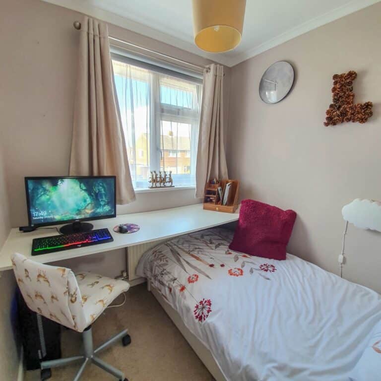 Take a Small Bedroom tour: this tidy space features a single bed, desk with computer, patterned chair, and cream-curtained window. Charming details like a wall clock and floral letter L complete the look.