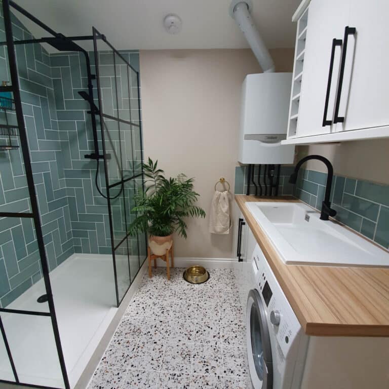 Modern bathroom and utility room with a glass shower, green tiled walls, washing machine, wooden worktop, sink, potted plant, towel ring, pet food bowl, and stylish blue-green splashback tiles—perfect for your next Utility Room Tour.