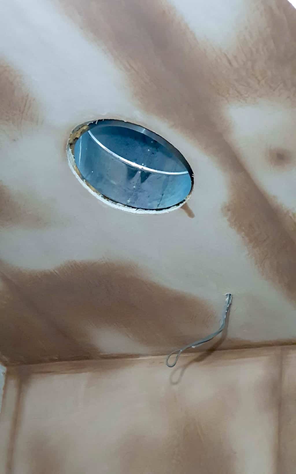 A ceiling with an unfinished circular hole reveals ductwork and a loose electrical wire, surrounded by patchy paint or plaster—ideal for installing a Solatube Sun Tunnel to light a room with no windows.