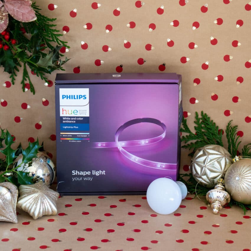 A Philips Hue lightstrip box and a smart bulb sit on a red polka dot background, surrounded by festive baubles and greenery—perfect home tech for your Christmas gift guide.