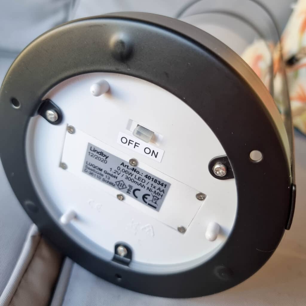 Close-up of the bottom of a solar powered lighting lamp showing a label, screws, battery compartment, and a black switch with positions labelled “OFF” and “ON.” The switch is currently set to ON. Perfect for pergola installations.