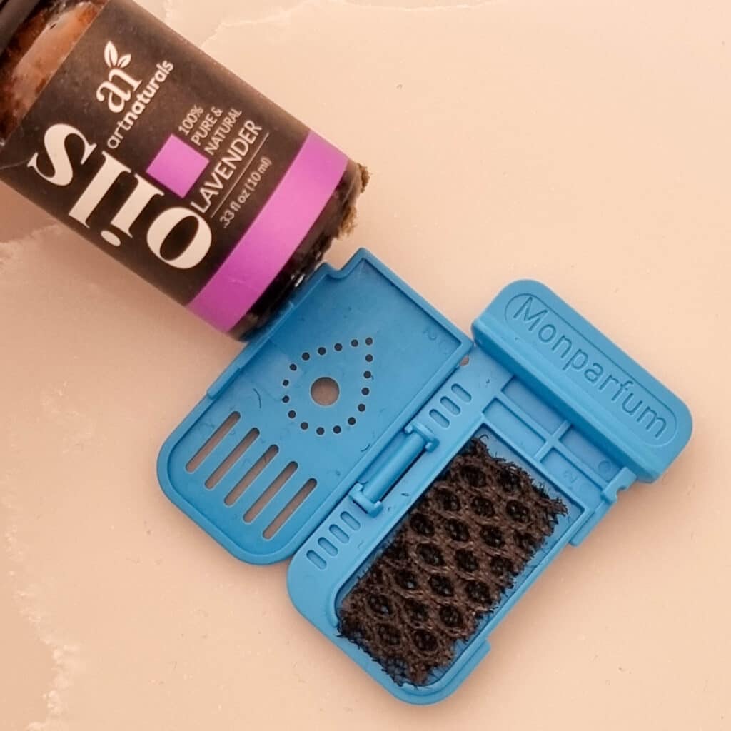 A small bottle of lavender essential oil lies next to an open blue Monparfum scent diffuser with a black sponge pad inside, both placed on a light-coloured surface—perfect for a calming touch after using your Tefal DT9530 Handheld Garment Steamer.