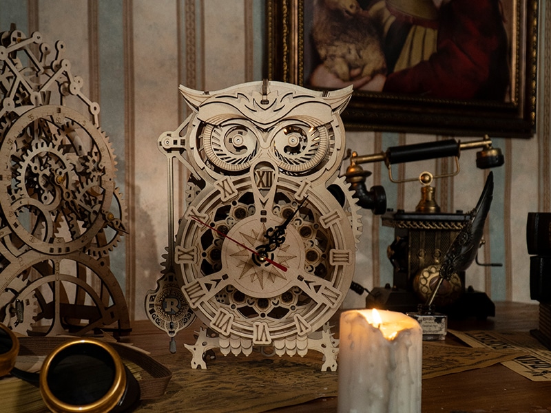A stylish puzzle of a wooden owl-shaped clock with Roman numerals sits on a cluttered desk, surrounded by steampunk-style gears, a candle, vintage telephone, goggles, and a framed painting in the background.