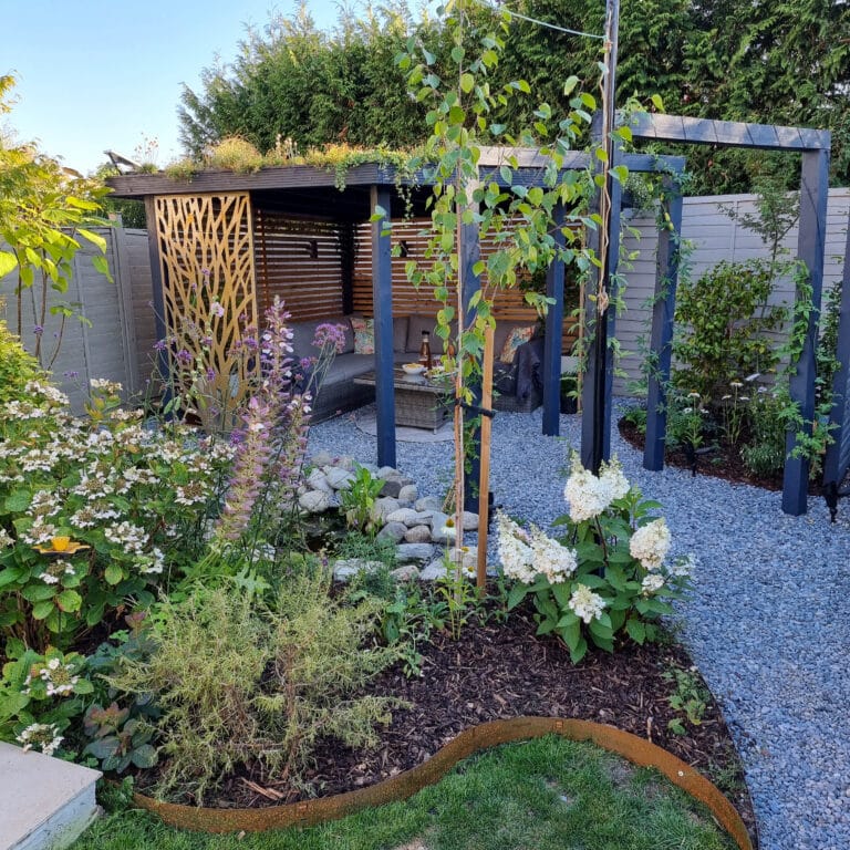 A landscaped garden with flowering plants, a gravel path, and a modern wooden pergola featuring a decorative screen—an inviting outdoor space that highlights current home renovation trends and enhances both beauty and property value.