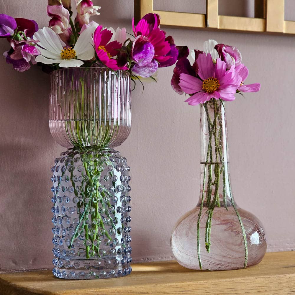 Two glass vases with pink and white flowers sit on a wooden surface. Perfect for brightening spaces during renovations, these elegant vases—with visible long green stems—let you enjoy a fresh look while you save money on décor.