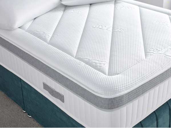 Close-up of a white mattress with a textured surface and grey trim, placed on a teal bed frame. Highlighting comfort, this setup is ideal for those seeking the Best Beds for Summer, featuring patterns and a handy fabric handle. White pillow peeks in at the corner.