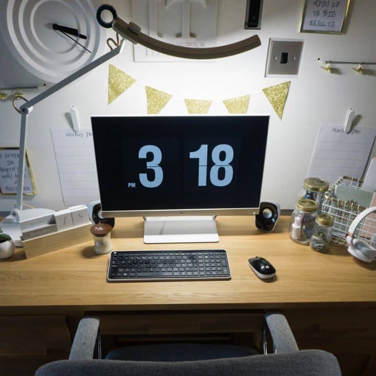 A tidy desk setup with a computer displaying the time 3:18 pm, a keyboard, mouse, lamp, coffee cup, and organised stationery. Decorative items and notes are pinned on the wall—ideal for tackling social media analytics or using Data365.