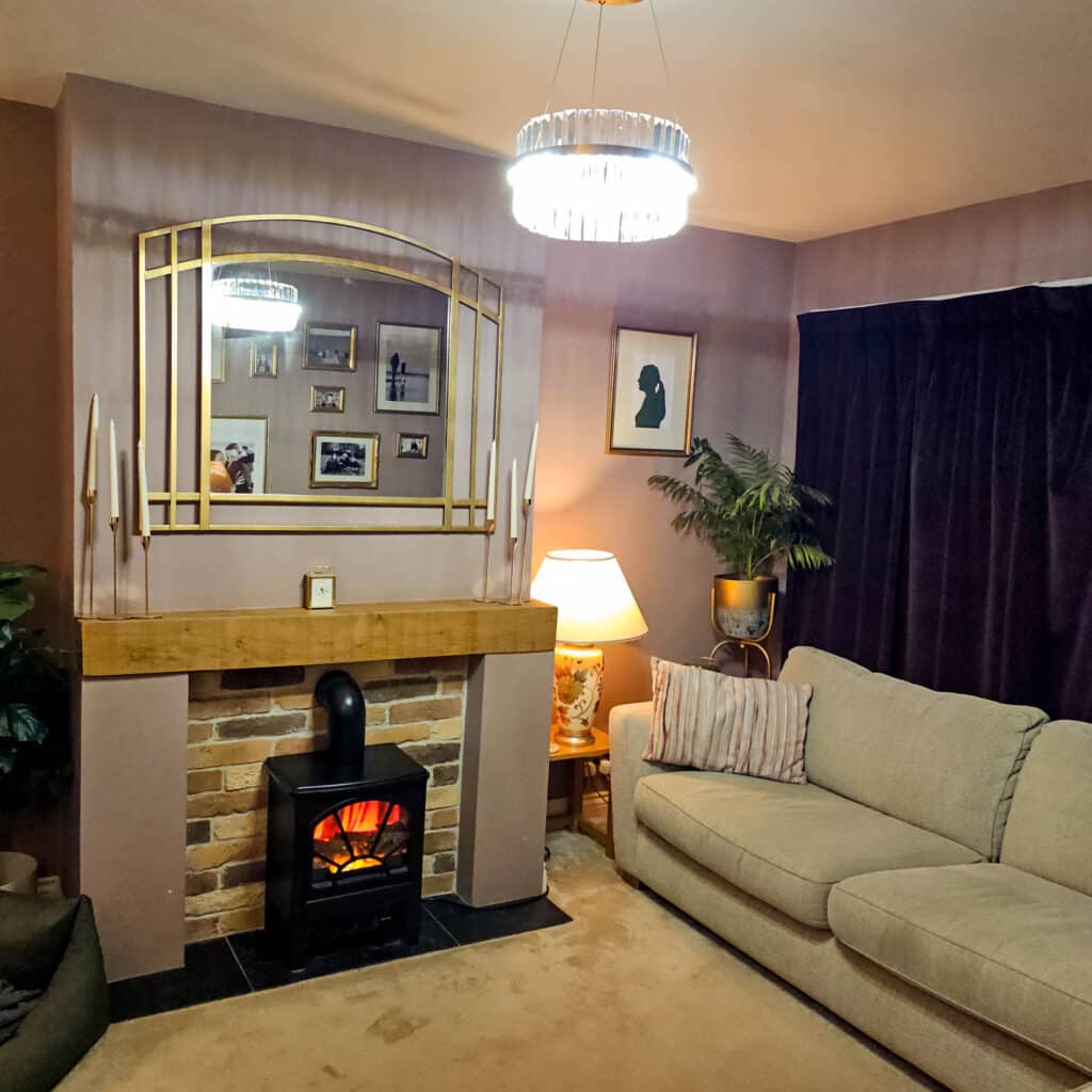 Cosy living room with a beige sofa, brick fireplace, electric stove heater, and warm lighting. A Brushed Gold Halo LED Pendant from Pagazzi Camburn serves as the perfect living room light, enhancing the inviting atmosphere.